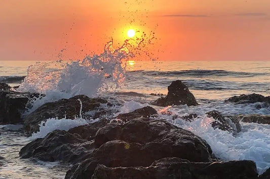 ocean wave crashing against rocks at sunset symbolising trauma alchemy, emotional release, and transformation