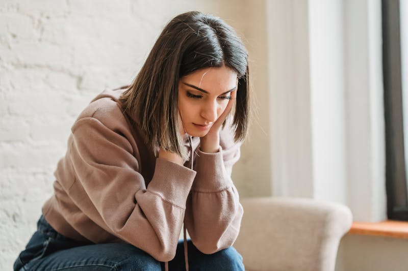 A highly sensitive woman sitting on a couch, looking upset and overwhelmed, reflecting emotional sensitivity
