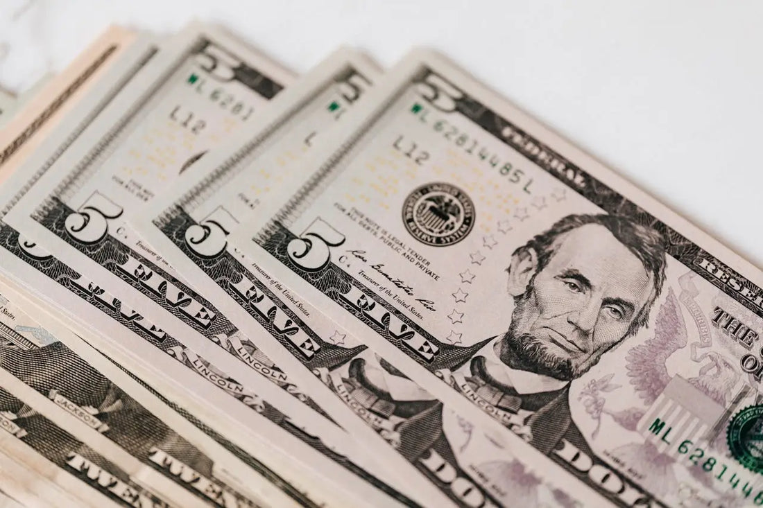 A stack of five-dollar bills on a table, symbolizing the unseen economy of value exchange and spiritual growth.