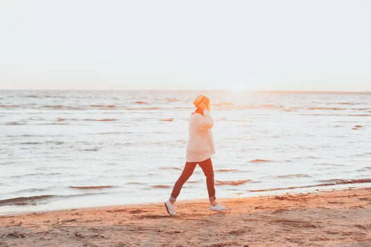 A woman walking alone on a seashore at sunrise, reflecting on life and mindfulness, representing levels of consciousness and inner awareness