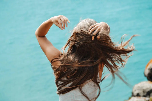 A woman with medium-length hair facing the camera, gently touching her hair with one hand, wearing a calm, contemplative expression