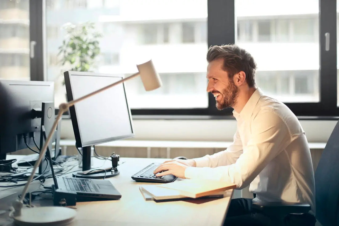 man in white shirt sitting at his desk smiling while working