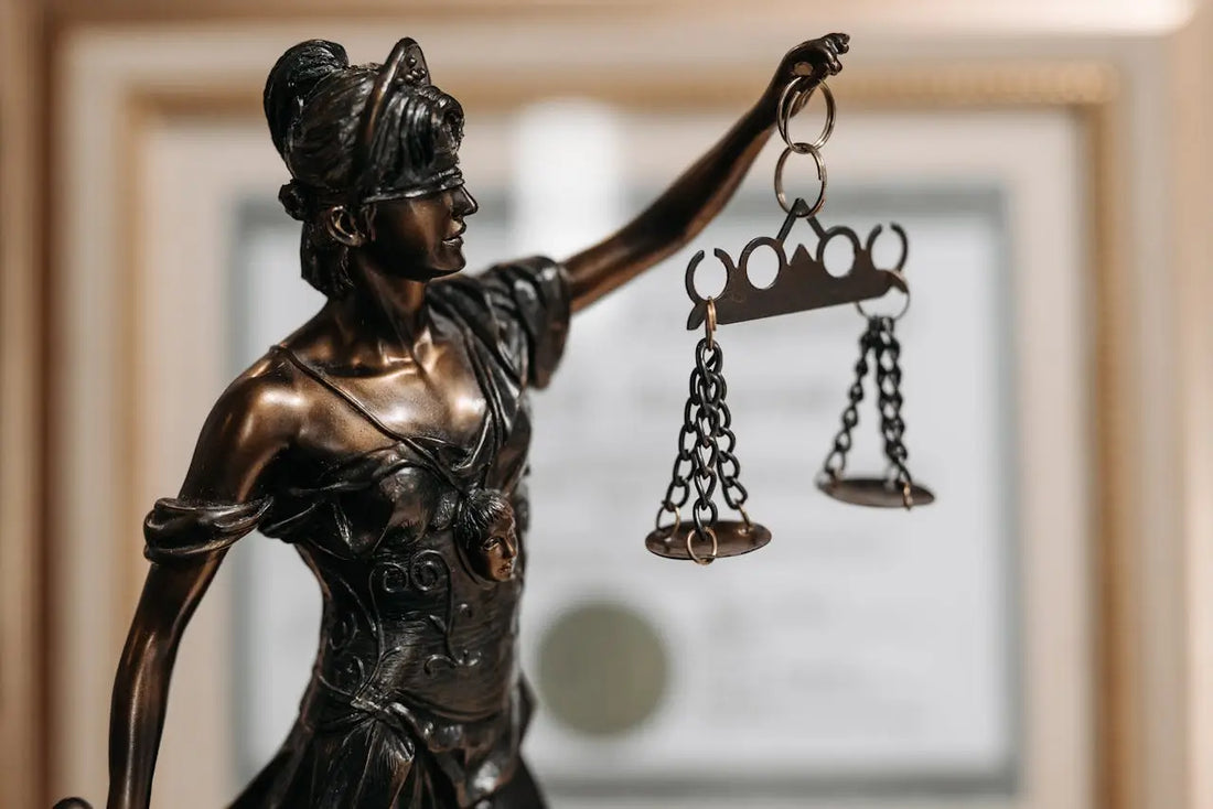 A bronze Lady Justice statue holding broken scales, symbolizing the universal law of imbalance.