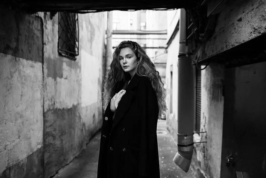 A young woman in a coat stands alone in a narrow concrete alley, symbolizing quiet strength and presence in a world of noise and attention-seeking