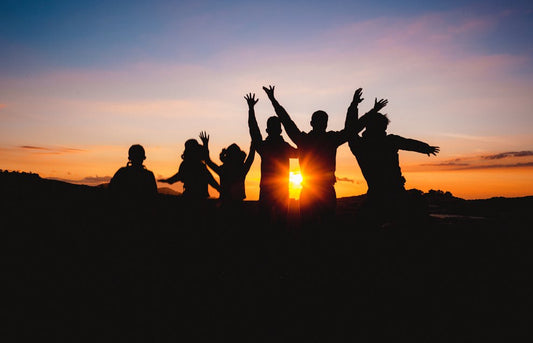 A group of people raising hands in golden hour on top of the hill