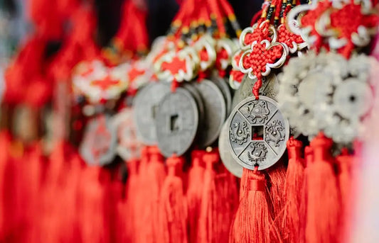 A close-up of several ancient-looking Chinese coins tied together with red knotted ropes and tassels.