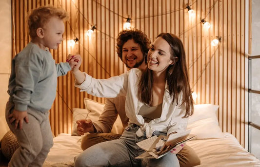 Parents engaging in authoritative parenting by playing and laughing with their child in bed, fostering warmth and guidance