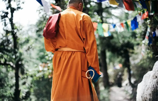 Tibetan monk in yellow robes walking on a mountain path, surrounded by sunlight and trees, conveying serenity and spiritual journey.